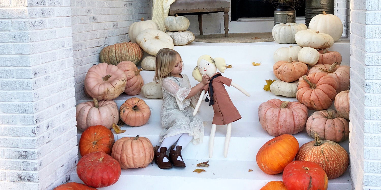 girl playing with doll on pumpkin lined stairs